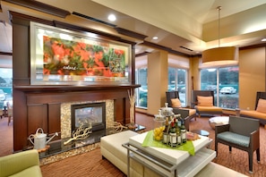 A hotel lobby with a fireplace, seating area, and a large window offering a view of the parking lot.
