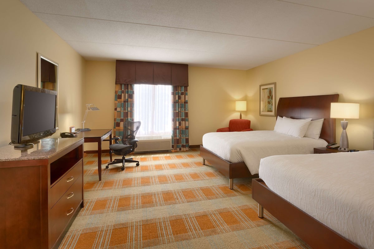 A hotel room with two beds, a desk with a computer, a chair, and a television.