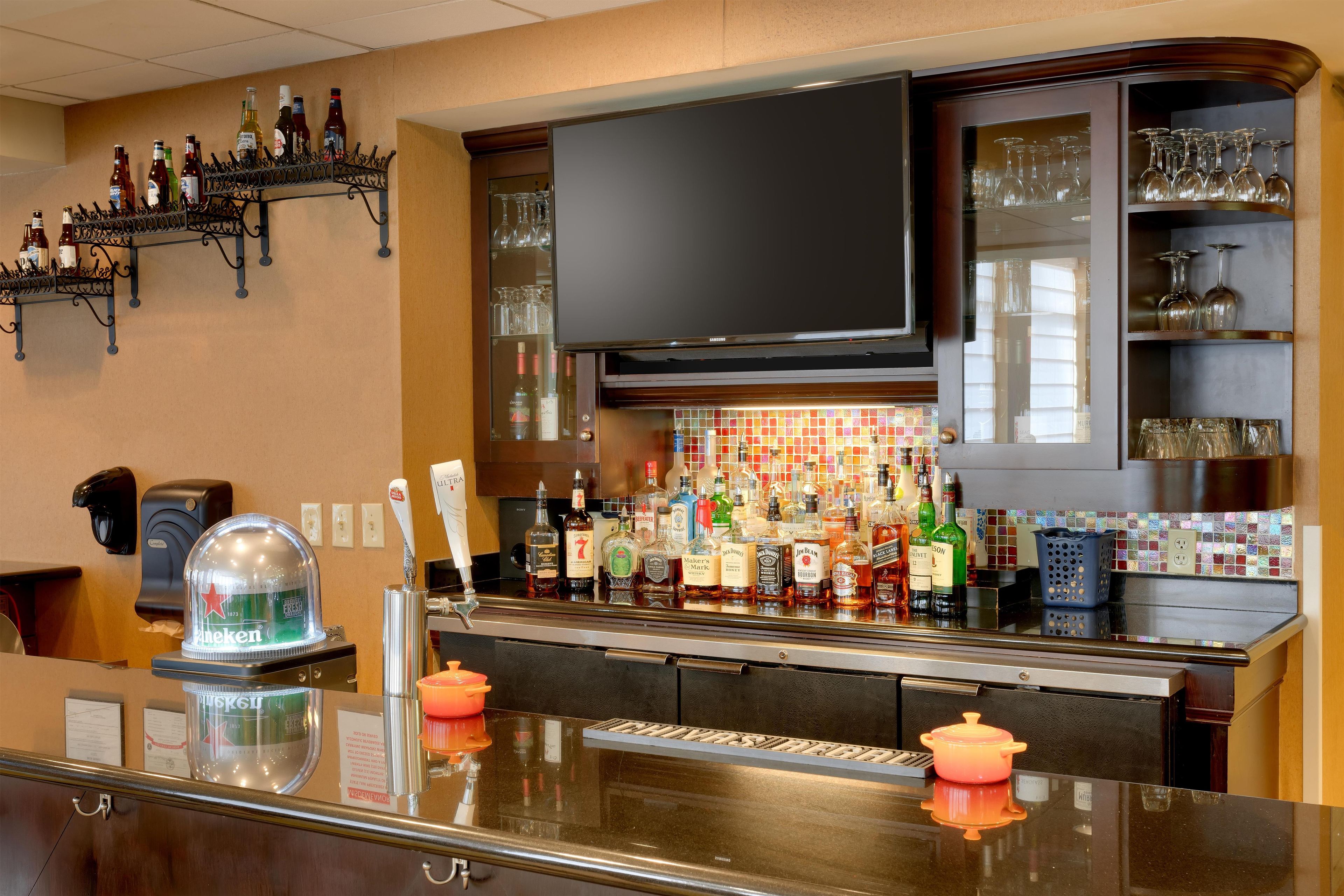 A bar area with a variety of liquor bottles, a television above the bar, and shelves with glasses.