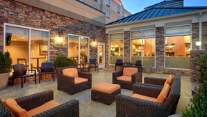 A hotel patio with wicker furniture, stone walls, and large windows. - Hilton Garden Inn Clarksville (Clarksville)