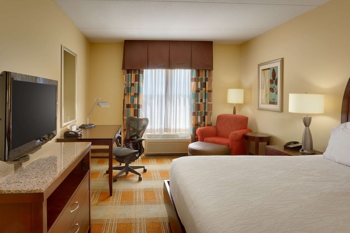A hotel room with a bed, desk, chair, television, and a window with curtains.