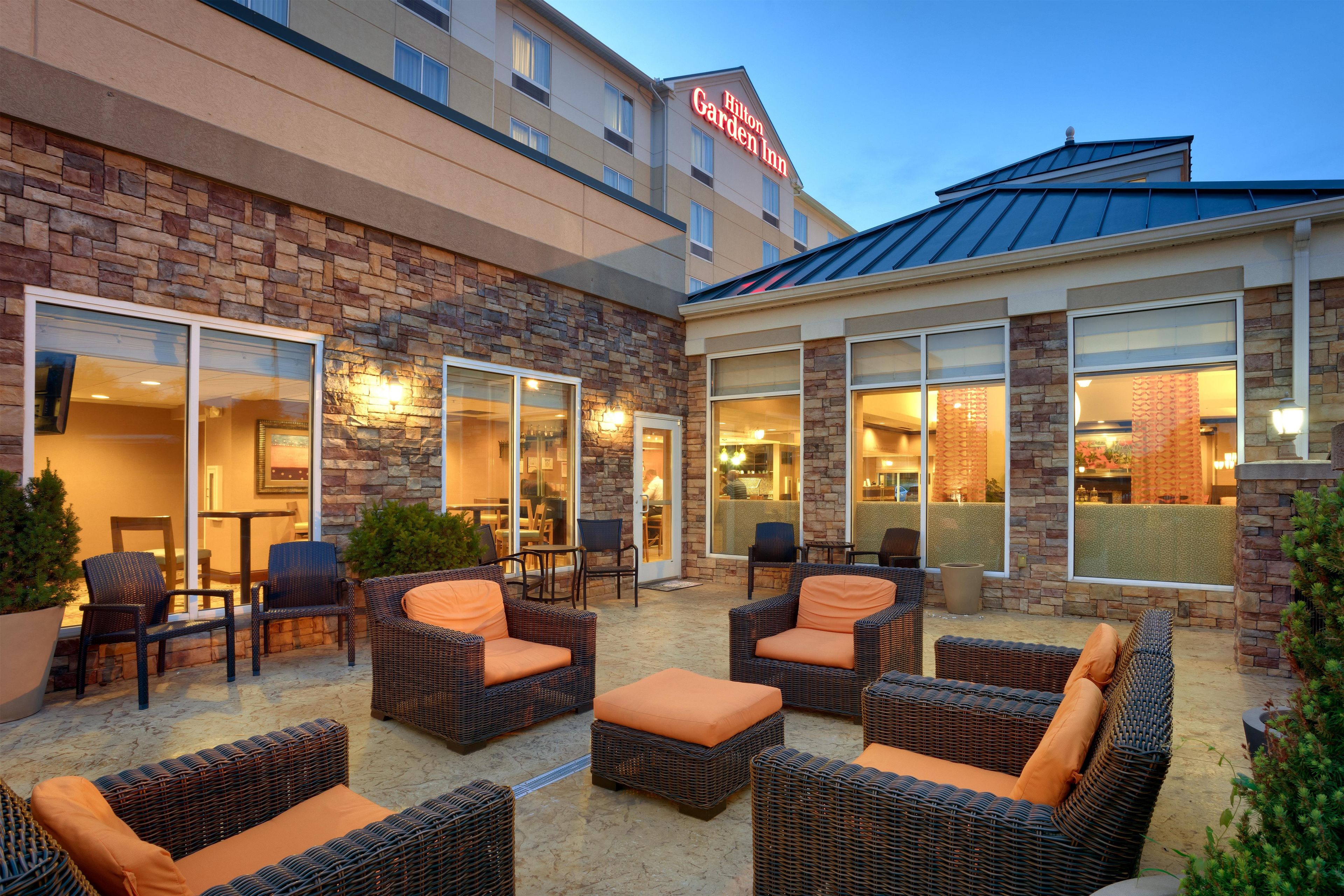 A hotel exterior with outdoor seating, stone facade, and a visible restaurant area.