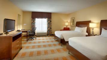 A hotel room with two beds, a desk with a computer, a chair, and a television.