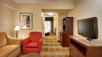 Une chambre d’hôtel avec un canapé, un fauteuil, une télévision et un tableau au mur.