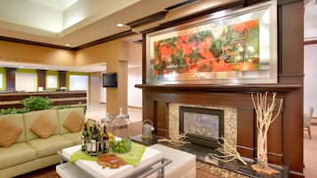 A hotel lobby with a fireplace, a sofa, a coffee table with bottles, and a television mounted above the fireplace.