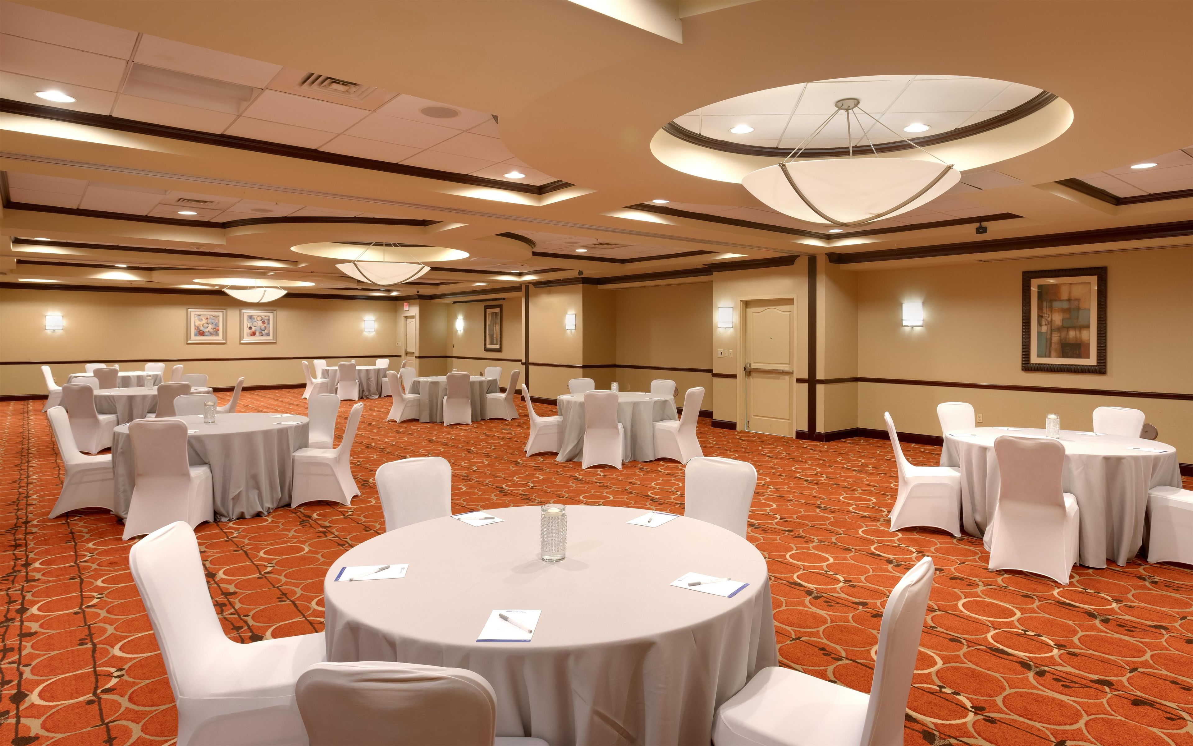 Un salón de conferencias con mesas redondas, sillas blancas y suelo alfombrado.