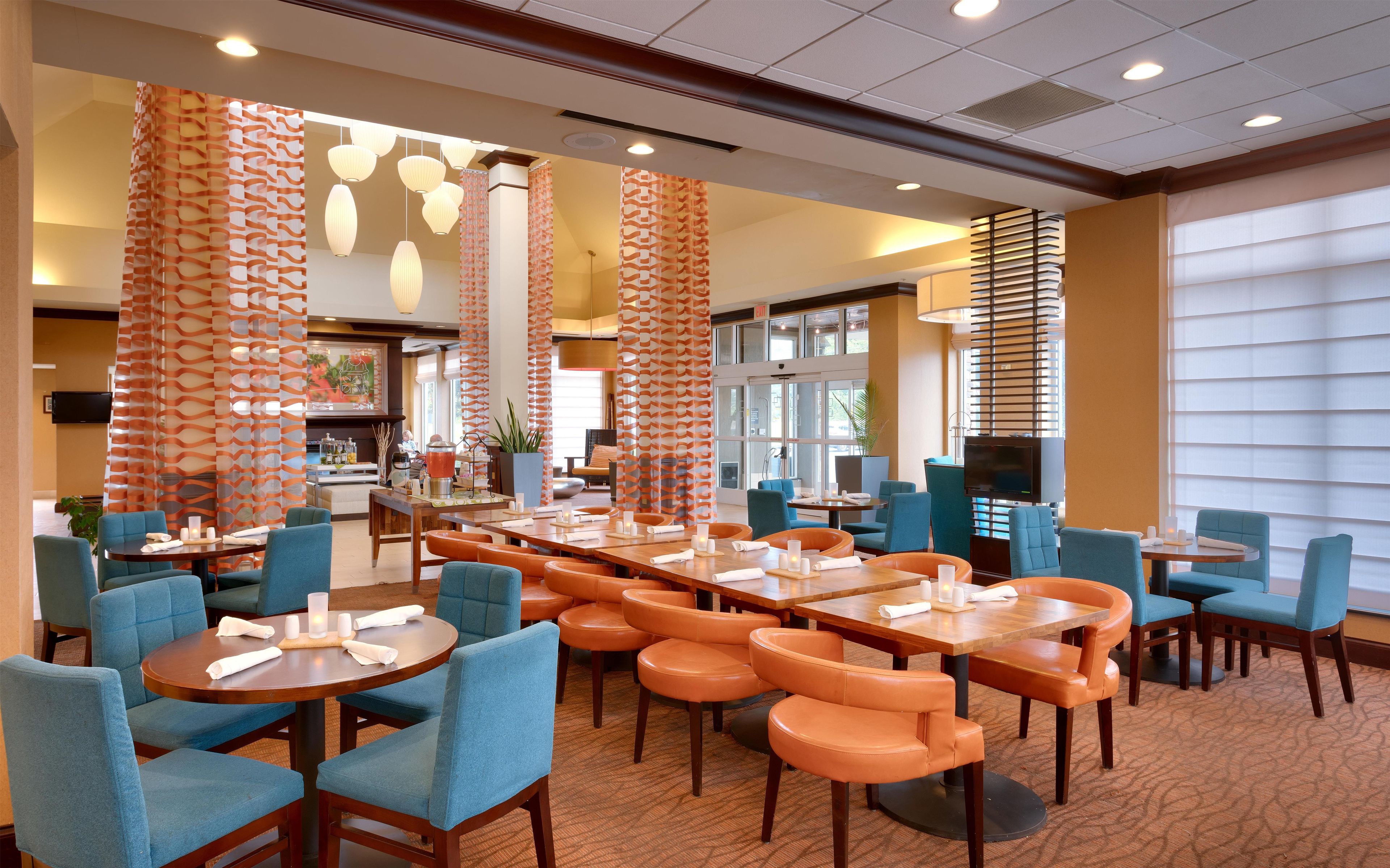 A hotel dining area with multiple tables and chairs, a television, and a large window.