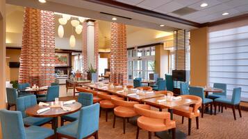 A hotel dining area with multiple tables and chairs, a television, and a large window.