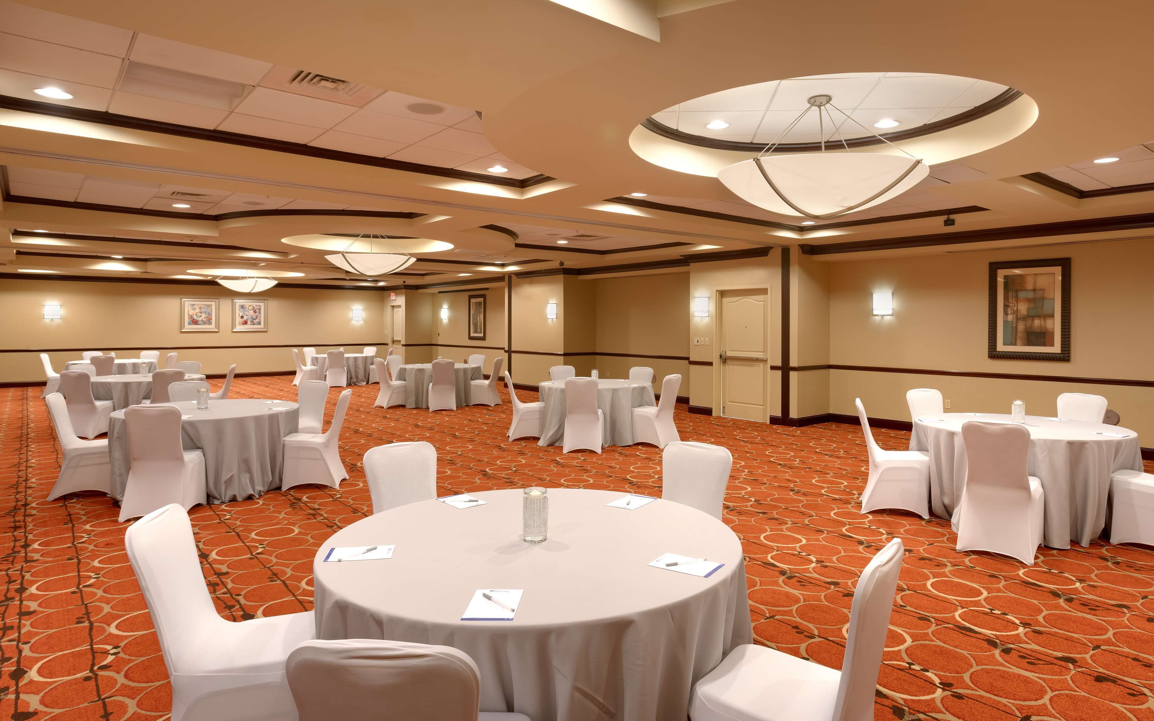 A conference room with multiple round tables, white chairs, and a patterned carpet.