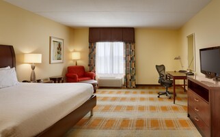 A hotel room with a bed, a desk with a computer, a chair, a lamp, a television, and a window with curtains.