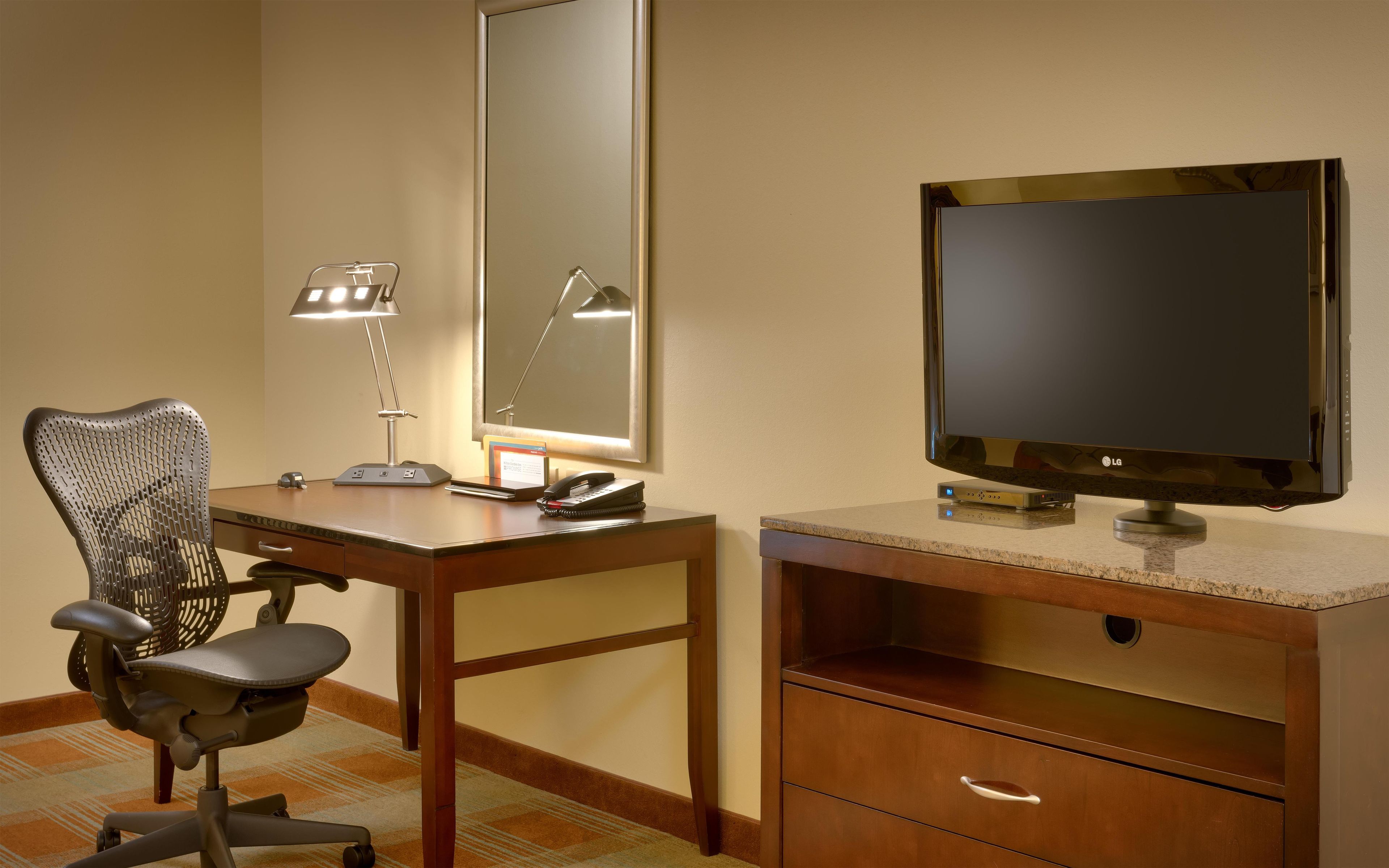 Habitación de hotel con escritorio, silla, espejo y televisión.