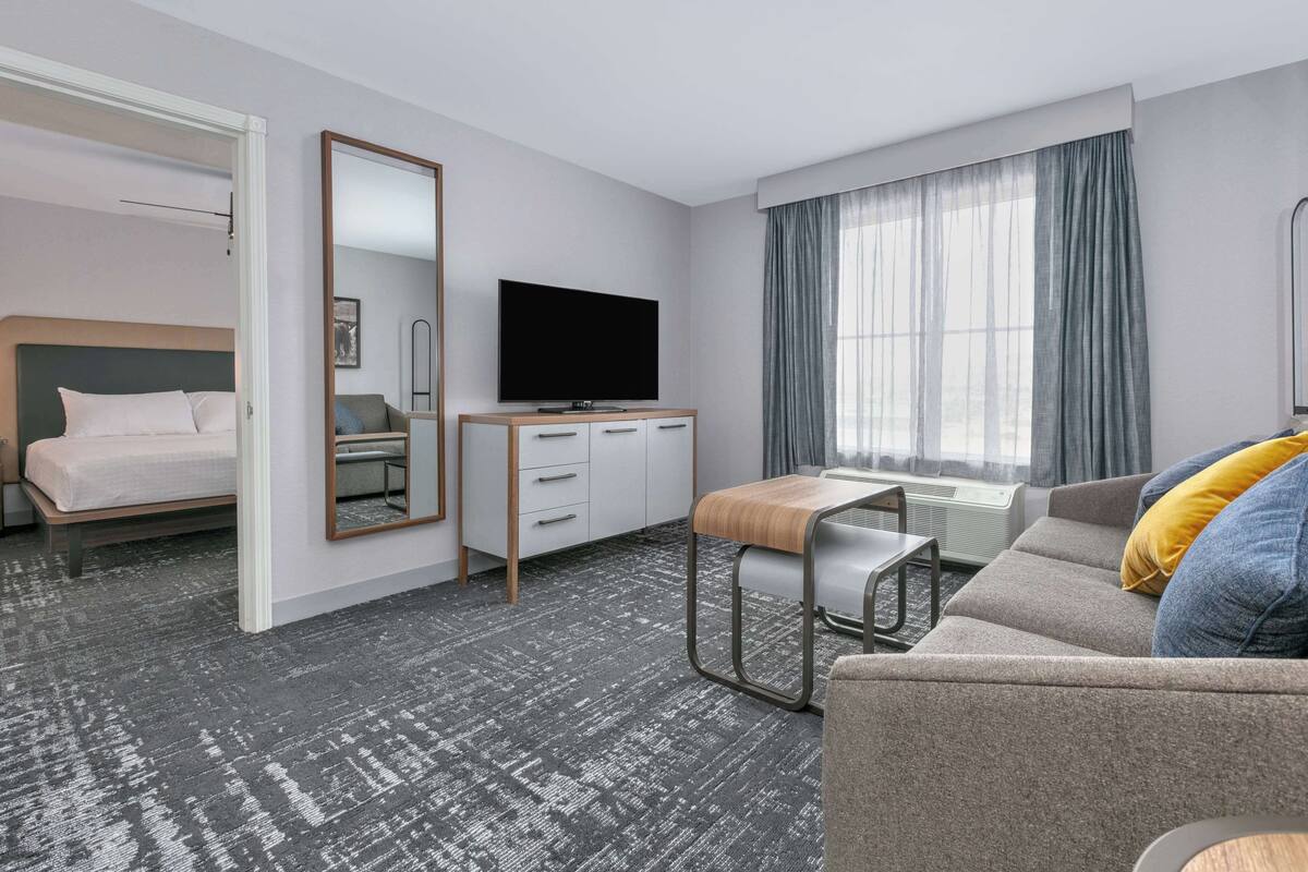 Een hotelkamer met een bed, een televisie, een bank, een bureau en een raam met gordijnen.
