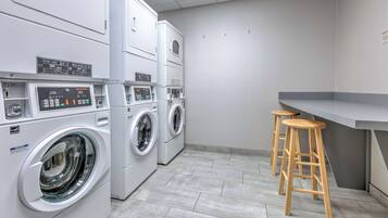 Une buanderie avec des lave-linge et des sèche-linge superposés, un petit coin bar avec des tabourets et un sol carrelé.