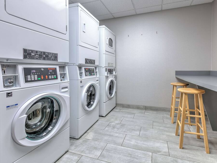 Une buanderie avec des lave-linge et des sèche-linge superposés, un petit coin bar avec des tabourets et un sol carrelé.
