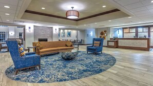 Un hall d’entrée avec un tapis à motifs bleus, un canapé marron et deux fauteuils bleus.
