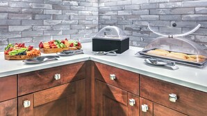 Un buffet proposant une variété de fruits et de légumes, un appareil pour maintenir les plats au chaud et un présentoir à pain.