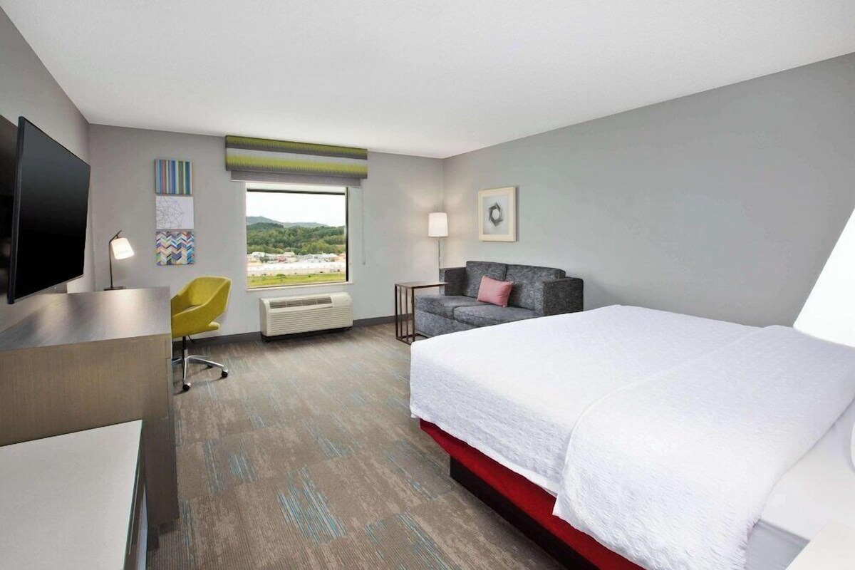 Habitación de hotel con cama, escritorio, silla, televisión y ventana con vista.