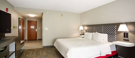 A hotel room with a large bed, bedside tables, a desk, and a television.