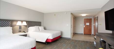 A hotel room with two beds, a desk, a chair, a TV, and a door leading to a hallway.