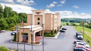 A Hampton Inn hotel with a parking lot, a red carpet entrance, and a view of the surrounding greenery and hills.