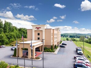 A Hampton Inn hotel with a parking lot, a red carpet entrance, and a view of the surrounding greenery and hills.