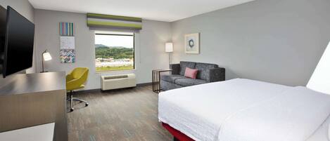 Habitación de hotel con cama, escritorio, silla, televisor y ventana con vista a la playa.