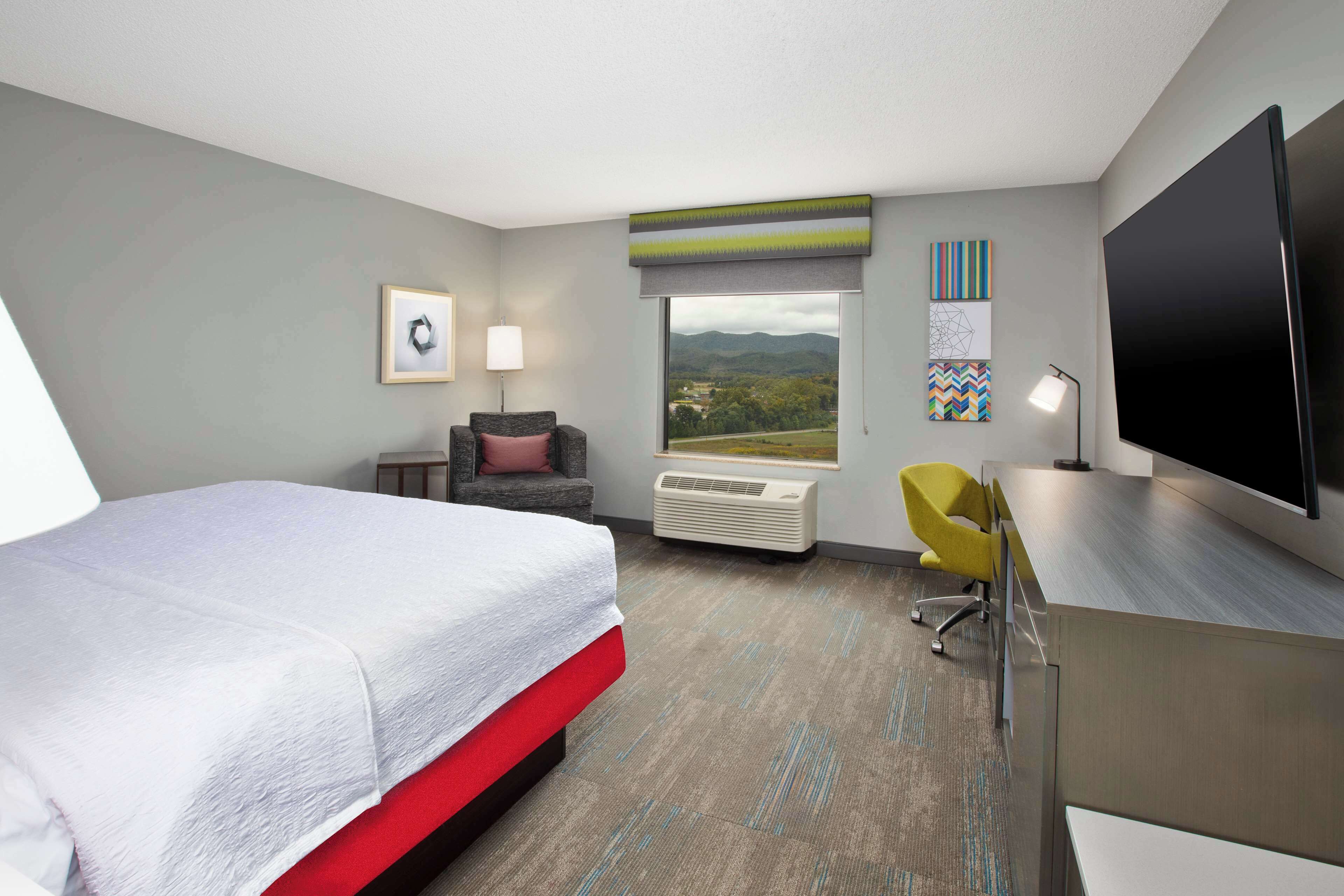 Une chambre d’hôtel équipée d’un lit, d’un bureau, d’une chaise, d’une télévision et d’une fenêtre donnant sur un paysage agréable.