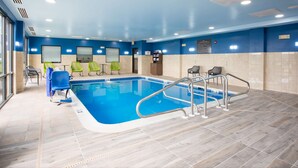 An indoor swimming pool with a blue and white tiled floor, green chairs, and a metal pool ladder.