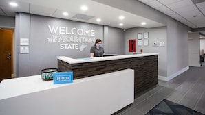 A reception desk with a "Welcome to the Mountain State" sign, a "Manager On Duty" sign, and a "Hilton Honors" sign. - Hampton Inn Elkins (Elkins)