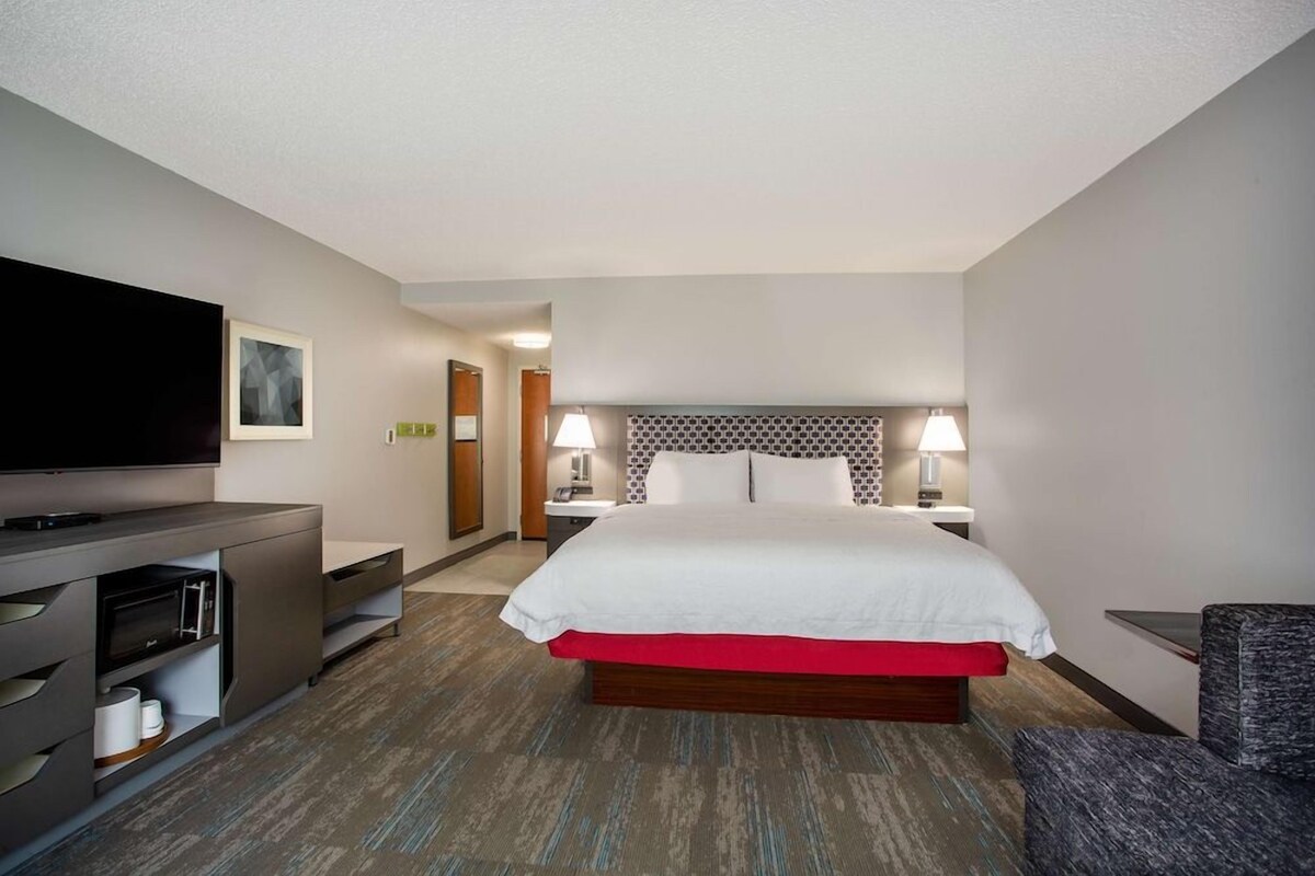 Habitación de hotel con una cama, un televisor, un escritorio con lámpara y una silla.