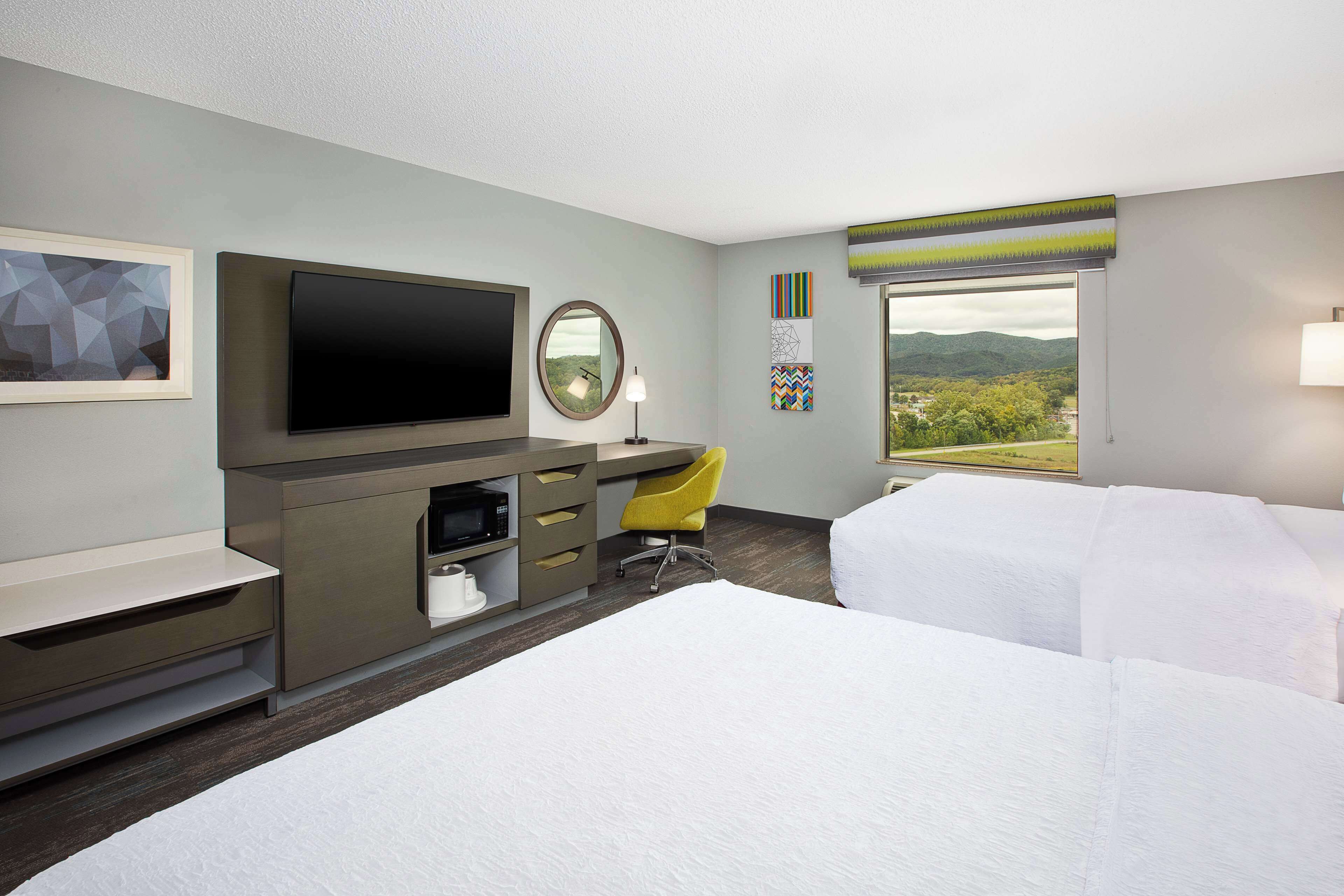 Une chambre d’hôtel comprenant un lit, un bureau avec un téléviseur à écran plat, une chaise et une fenêtre donnant sur l’extérieur.
