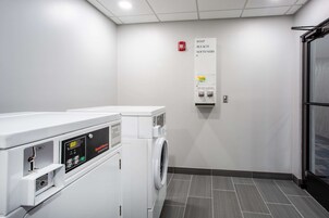 A laundry room with a washing machine, dryer, and a wall-mounted dispenser for soap, bleach, and softeners.