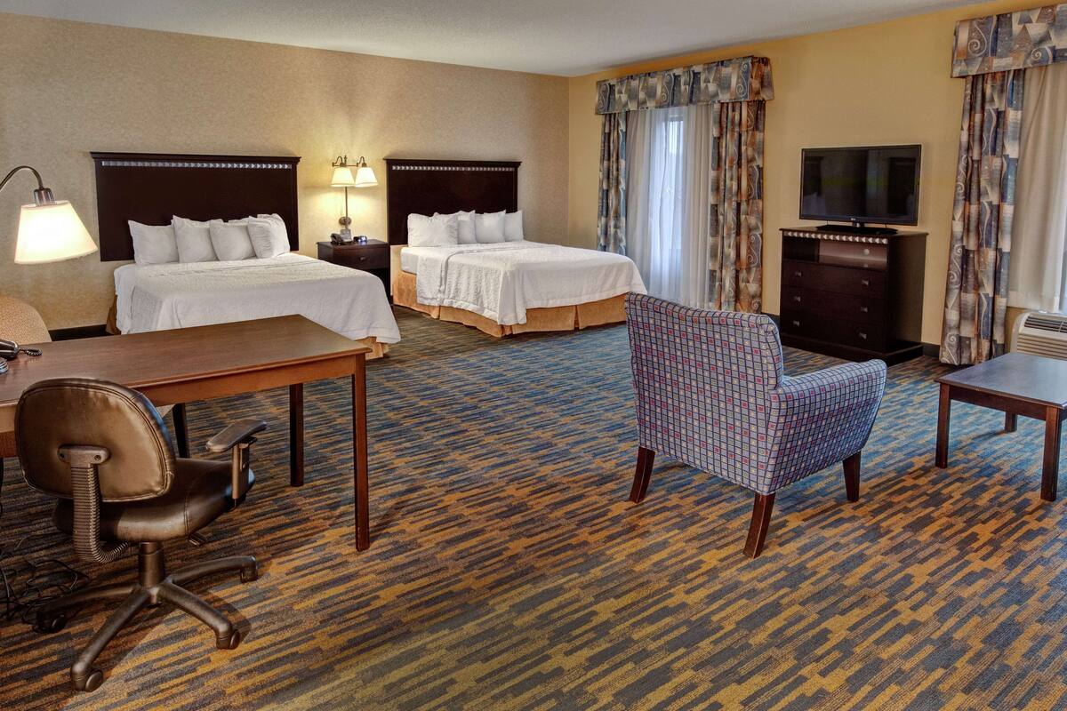 Quarto de hotel com duas camas, uma escrivaninha, uma cadeira, uma televisão e um aparador.