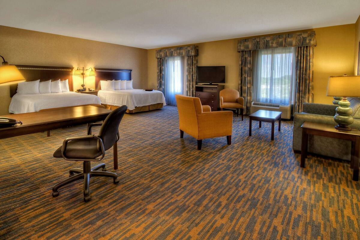 A hotel room with a large bed, a desk, a chair, a sofa, and a TV.