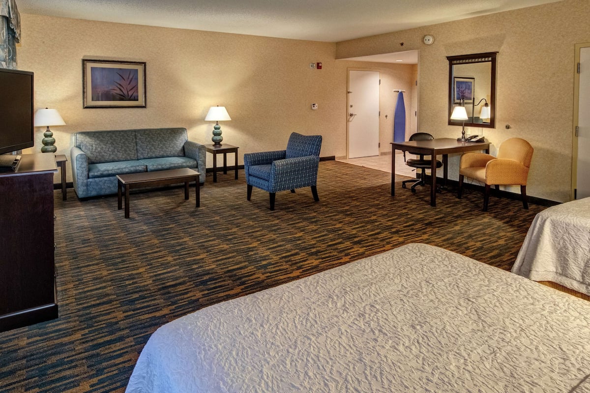 Quarto de hotel com uma cama grande, um sofá, duas poltronas, uma escrivaninha e uma televisão.