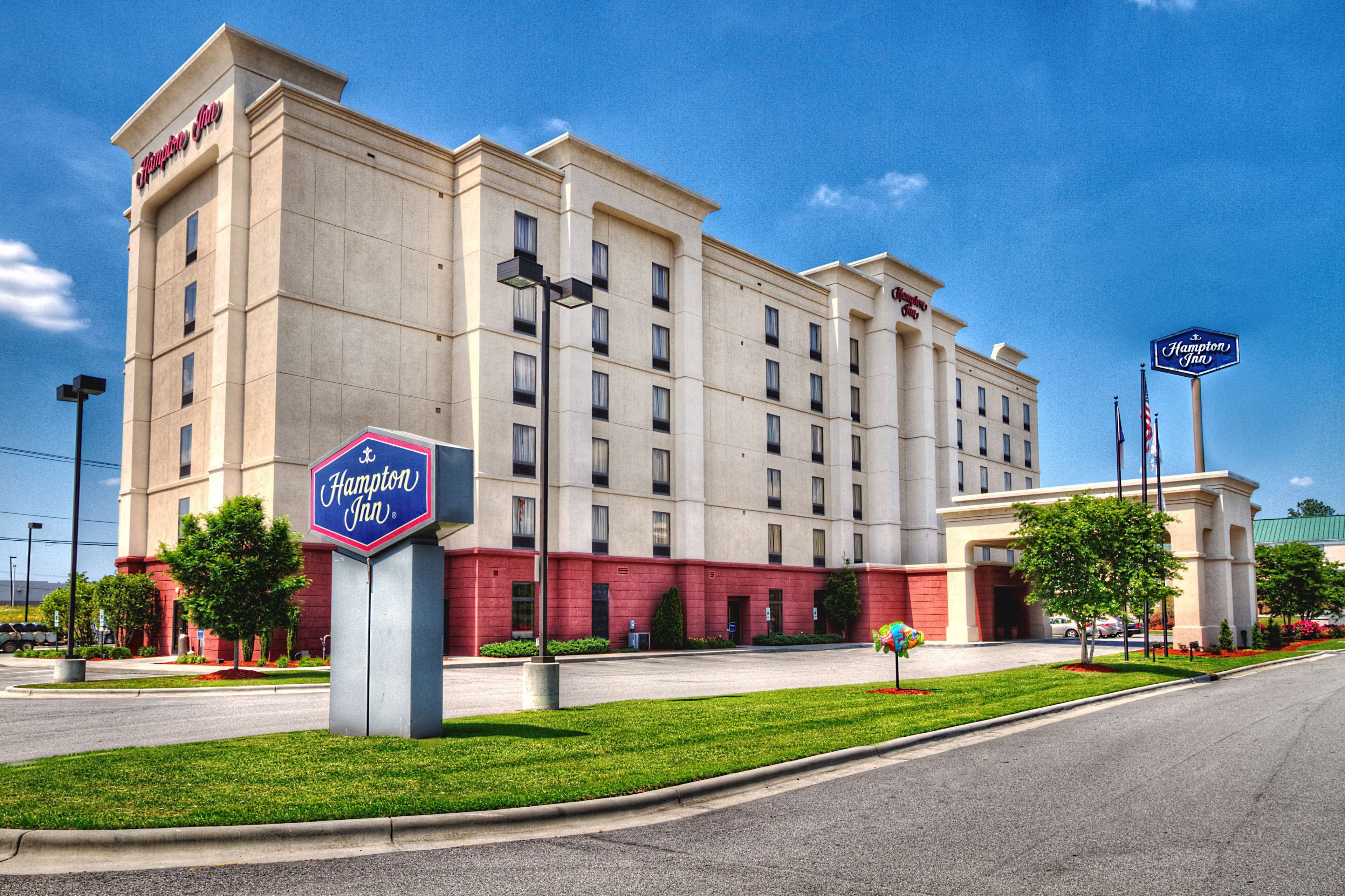 Um hotel Hampton Inn com fachada bege, várias janelas e seção inferior vermelha.