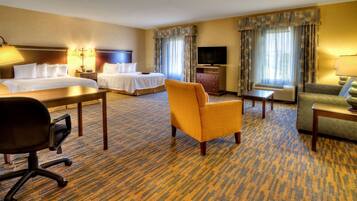 A hotel room with a king-sized bed, a sofa, a chair, a desk, a television, and a dresser.