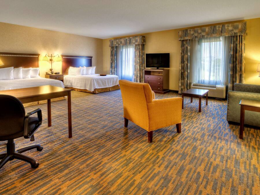 A hotel room with a king-sized bed, a sofa, a chair, a desk, a television, and a dresser.