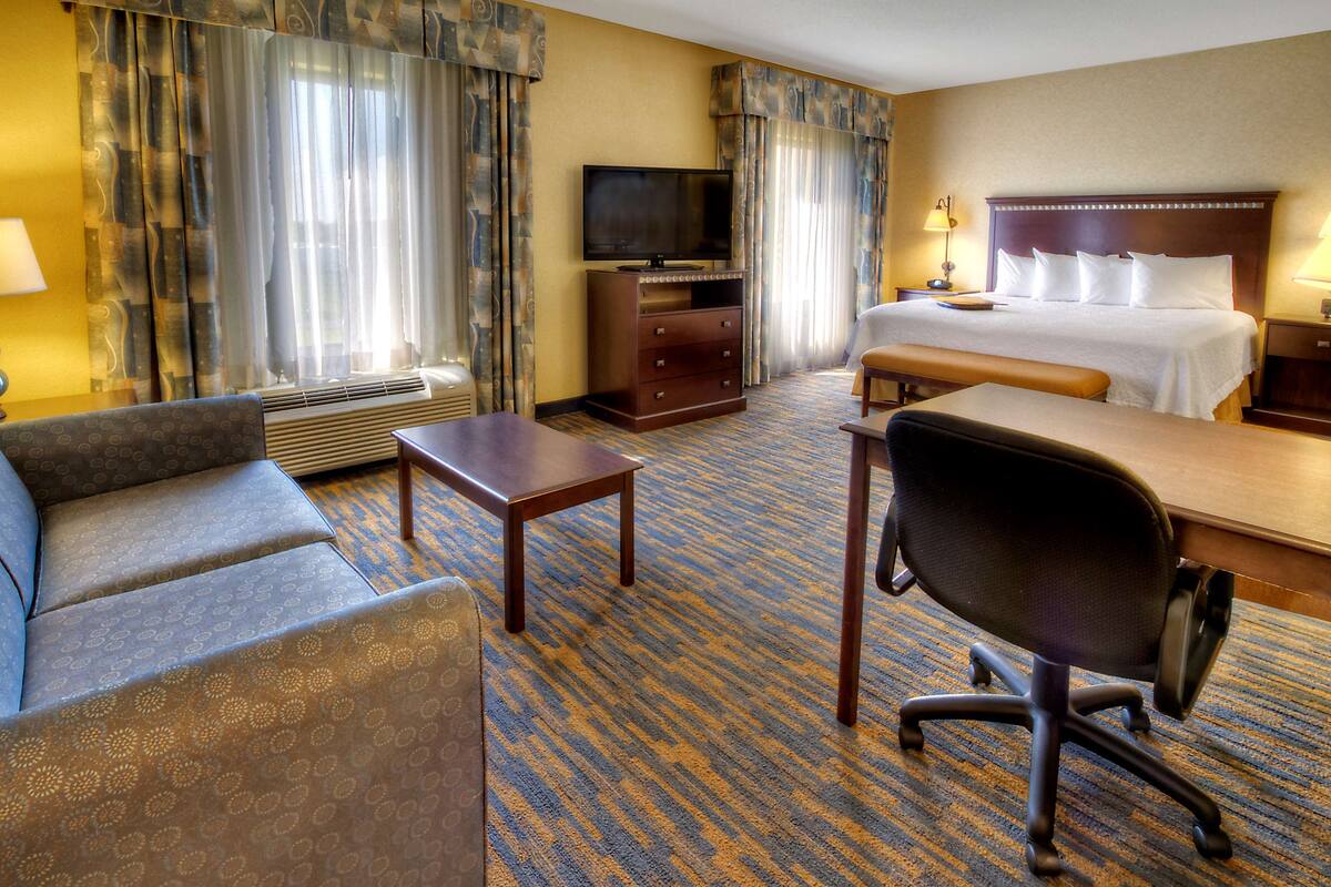 Quarto de hotel com cama, escrivaninha, cadeira, televisão e uma pequena mesa.