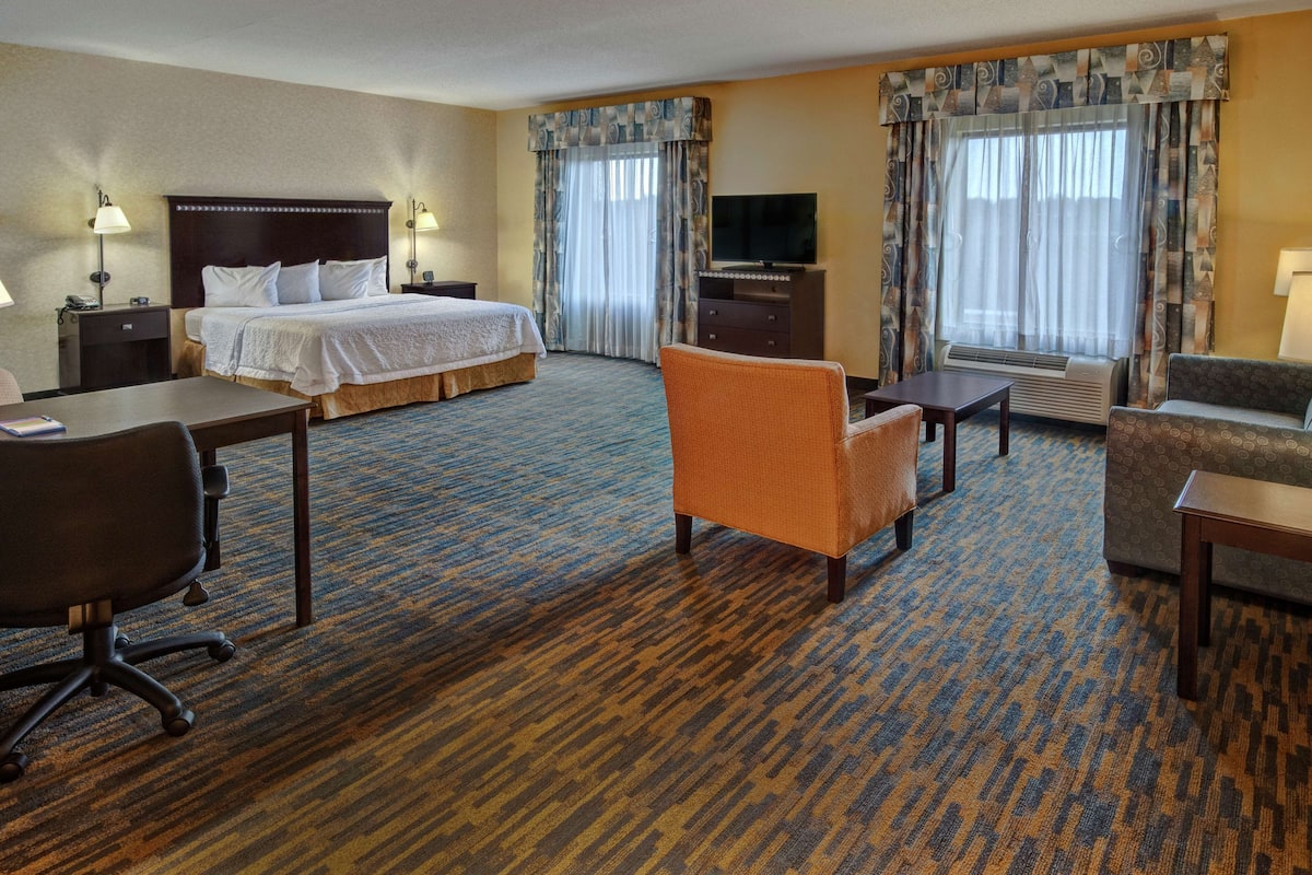 Quarto de hotel com uma cama grande, uma escrivaninha, uma poltrona laranja, um sofá e uma televisão.