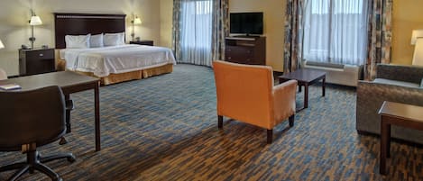 Habitació d'hotel amb un llit gran, una taula de treball, un sofà taronja, un divan i una televisió.