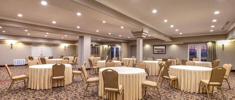 Une grande salle de conférence dotée de plusieurs tables rondes, de chaises de couleur beige et d’un tapis à motifs.