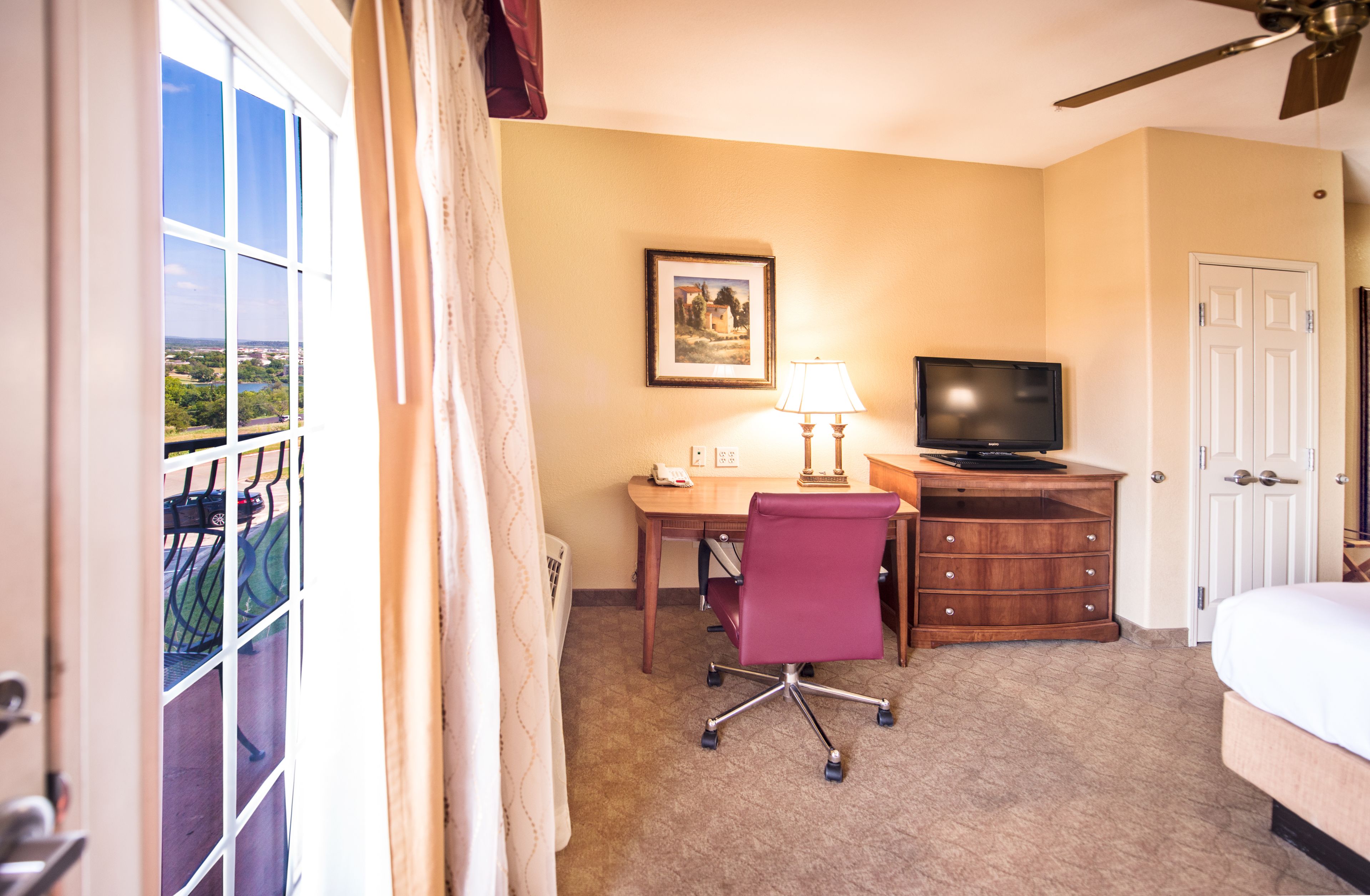 A hotel room with a desk, chair, television, and a bed.