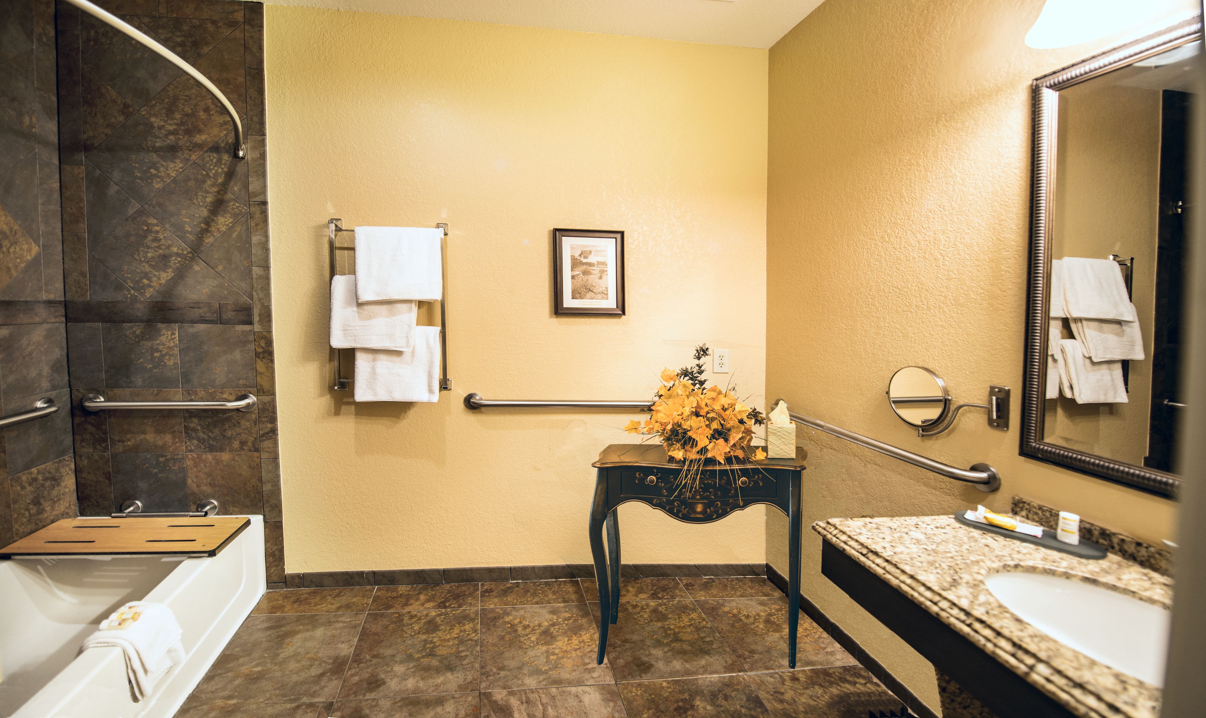 A bathroom with a bathtub, a sink, a vanity, a mirror, a towel rack, and a framed picture on the wall.