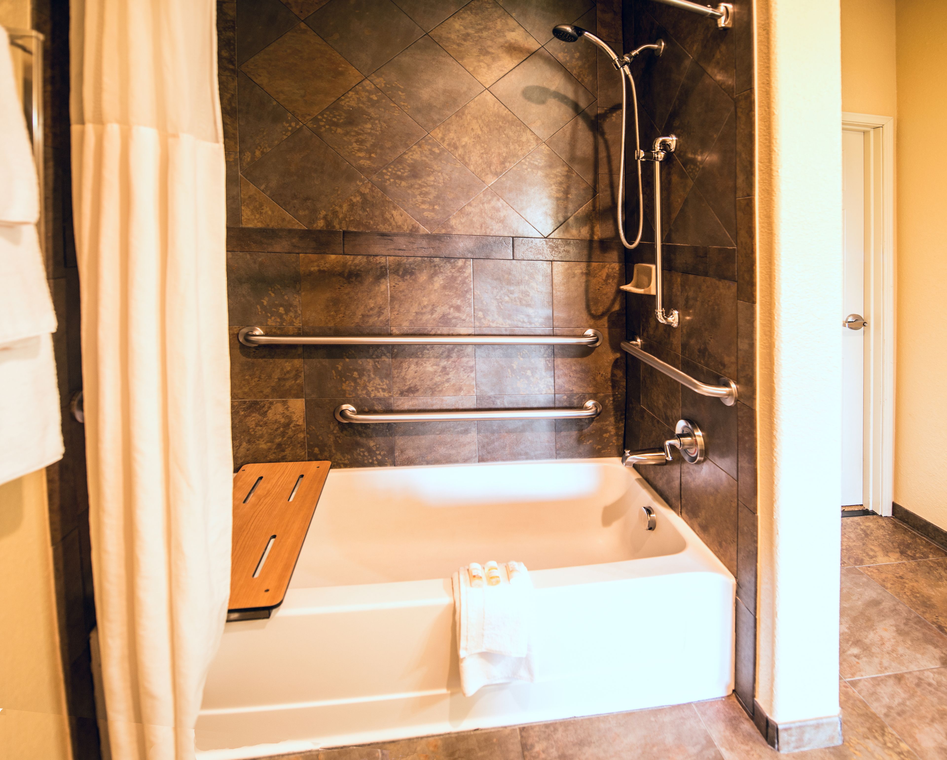 A modern bathroom with a walk-in shower, grab bars, and a wooden tray.