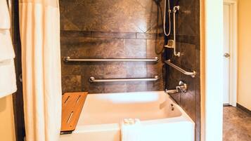 A modern bathroom with a walk-in shower, grab bars, and a wooden tray.