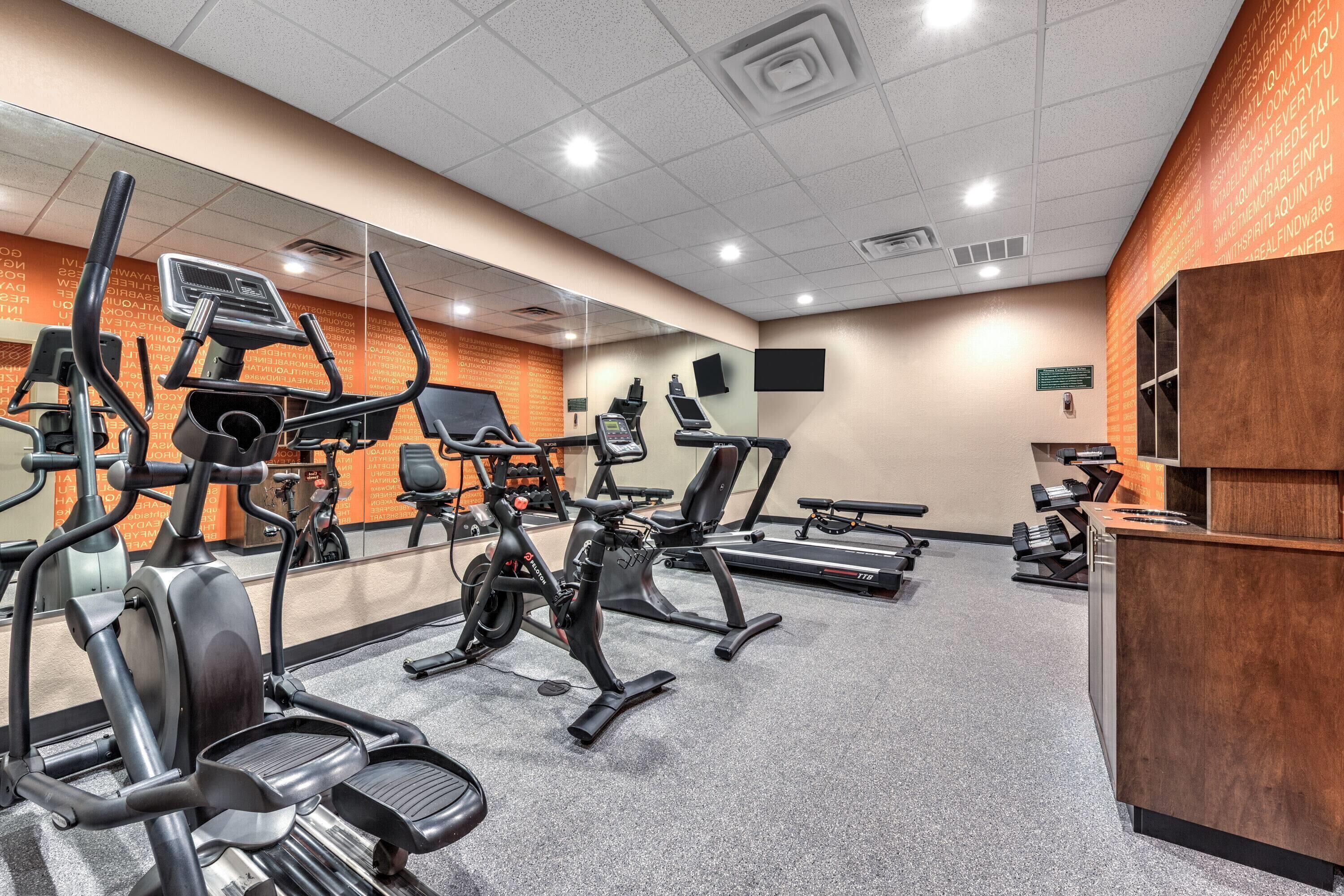 A gym with various exercise machines, a mirrored wall, and a reception desk.