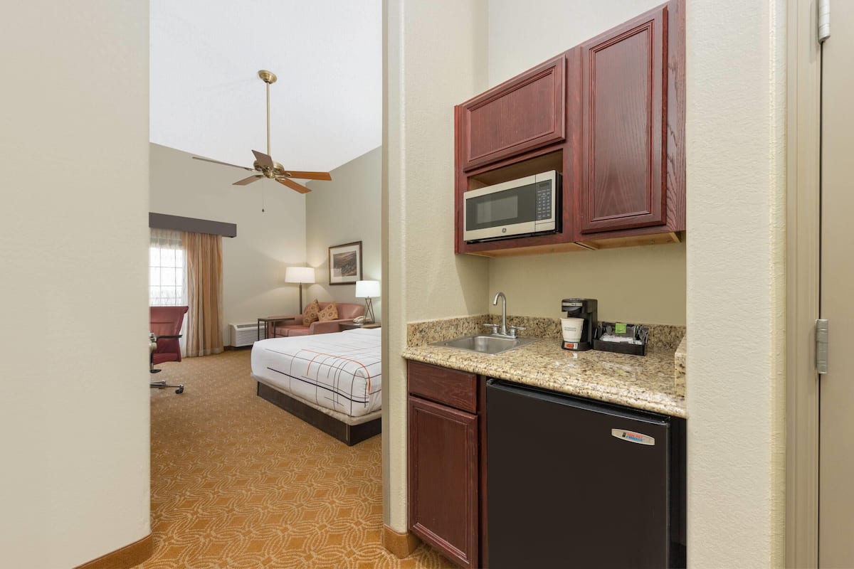 Een hotelkamer met een kitchenette, een bed, een plafondventilator en een badkamer met een rode stoel.