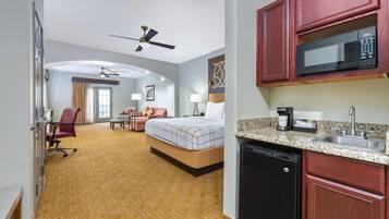 Habitación de hotel con cama, escritorio, silla, microondas, cafetera y lavabo.