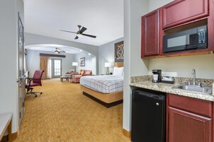 Habitación de hotel con cama, escritorio, silla, microondas, cafetera y lavabo.
